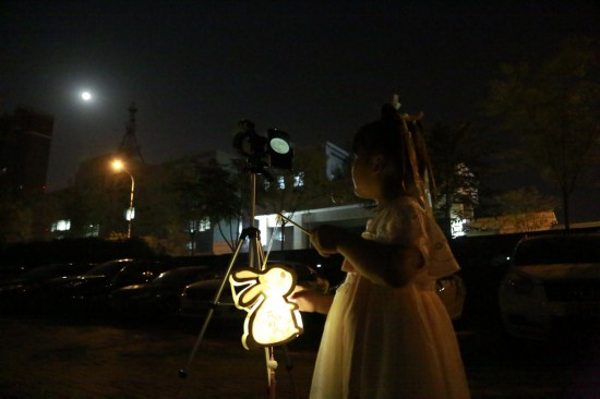 9月29日晚，在天津市津濱大道，一位身著漢服的小姑娘用天文望遠鏡觀看月亮。人民網記者 崔新耀攝